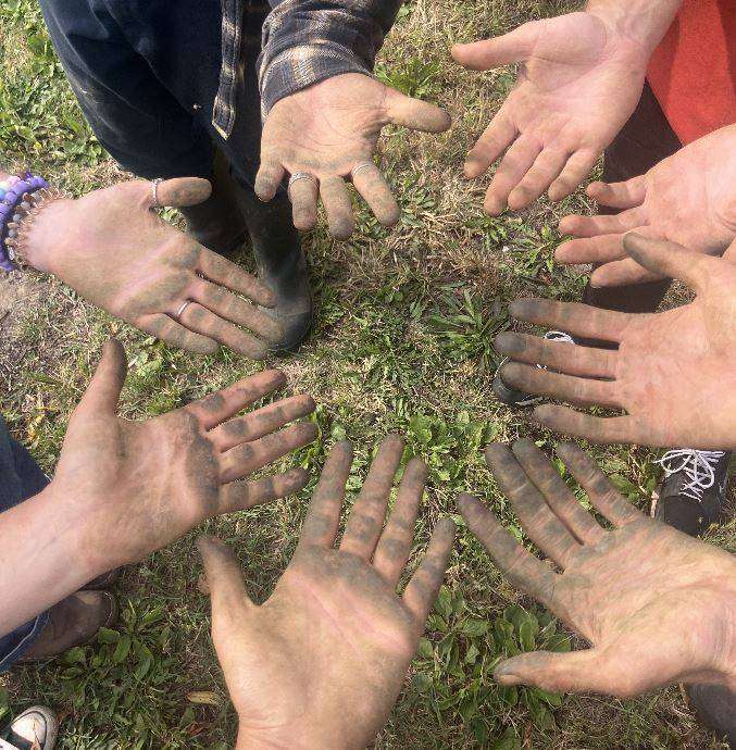 Volunteers holding their hands in a circle with tomato stains on them.